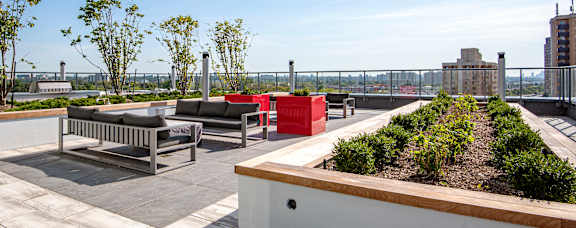 A rooftop patio with a bench, planter boxes, and trees.