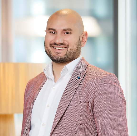 A man with a beard is wearing a pink blazer and a white shirt.