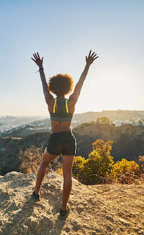 A person with arms raised stands on a rocky hilltop.
