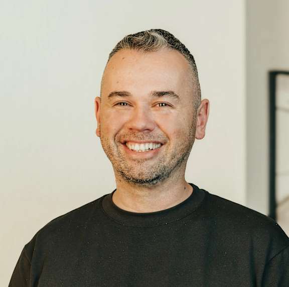 A man with a beard and short hair is wearing a black shirt and smiling.
