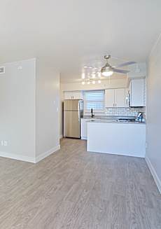 A spacious room with light wood flooring and a kitchen area in the background.