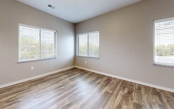 A room with wood flooring and three windows with blinds.