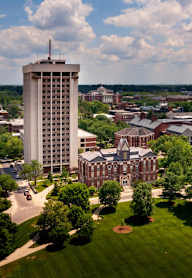 A tall building with a clock tower sits in the middle of a green campus.