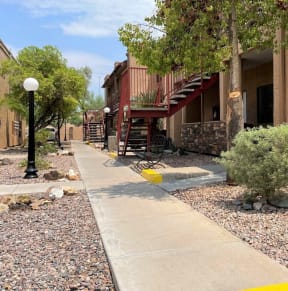 a sidewalk in front of a brick building with trees and bushes