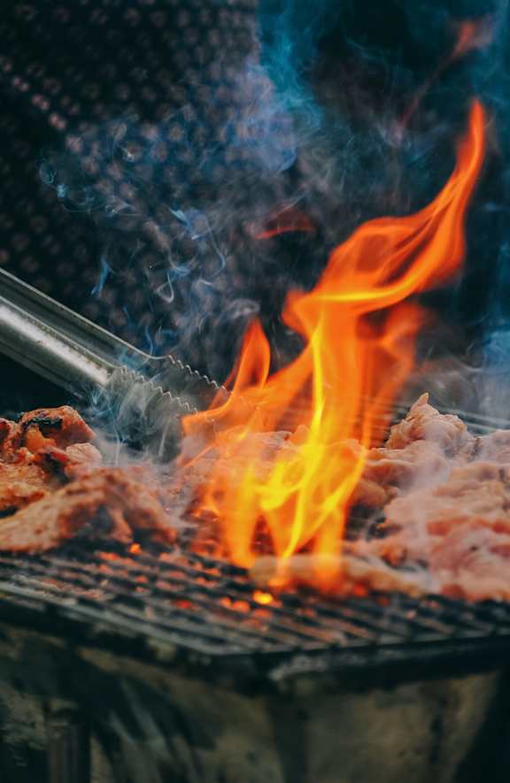 A person is grilling meat with a flame.