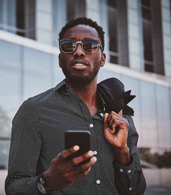 A man in a patterned shirt is holding a phone and adjusting his tie.