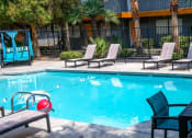 Thumbnail 11 of 23 - Fifteen 50 apartments near Las Vegas strip Community pool surrounded by tall gated fence, greenery, and patio loungers.
