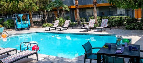 Fifteen 50 apartments near Las Vegas strip Community pool surrounded by tall gated fence, greenery, and patio loungers.