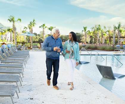 a man and a woman walking by a swimming pool with lounge chairs at Wharf 7 Apartments, South Carolina, 29492