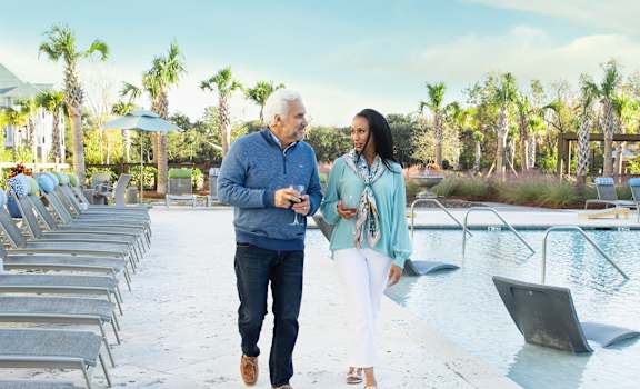 a man and a woman walking by a swimming pool with lounge chairs at Wharf 7 Apartments, South Carolina, 29492