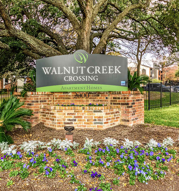 A sign for Walnut Creek Crossing Apartment Homes sits in front of a brick wall and a tree.