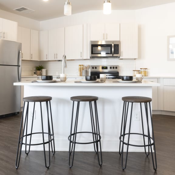 a kitchen with white cabinets and a counter with three bar stools
