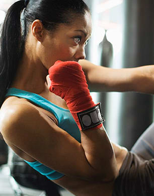 a woman in a blue shirt and red boxing gloves sits on the floor in a gym