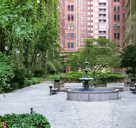 A woman in a beige sweater is standing on a bridge looking at the street below.at London Terrace Gardens, New York, 10011
