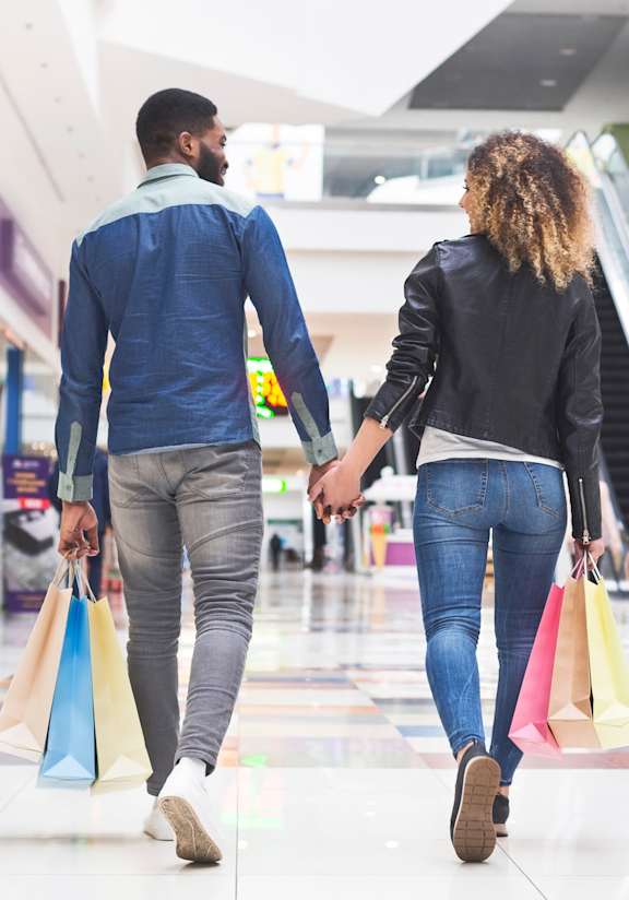 A man and a woman are walking hand in hand in a mall.