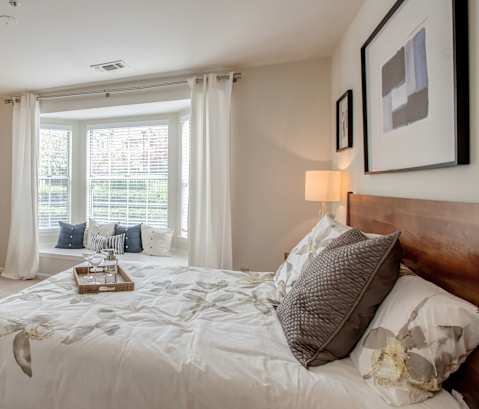 A bedroom with a large bed, a wooden dresser, and a window with curtains.