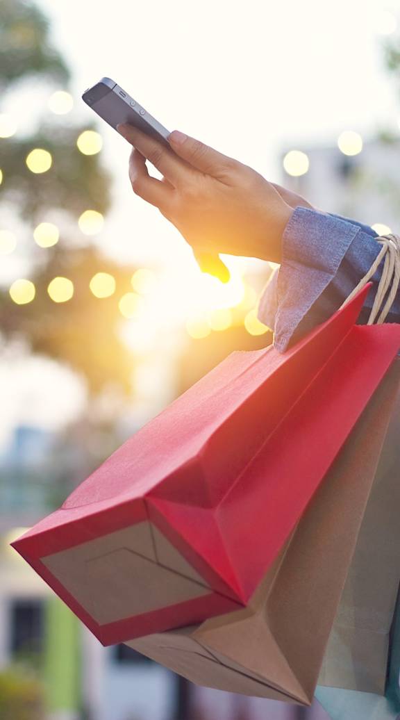 A person holding shopping bags and a phone in their hand. at Aero White Rock, Dallas, TX