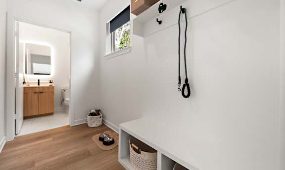 A white room with a wooden floor and a white wall with a black plant hanger on it.