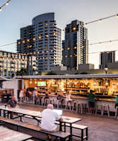 people sitting at tables outside of a restaurant with buildings in the background