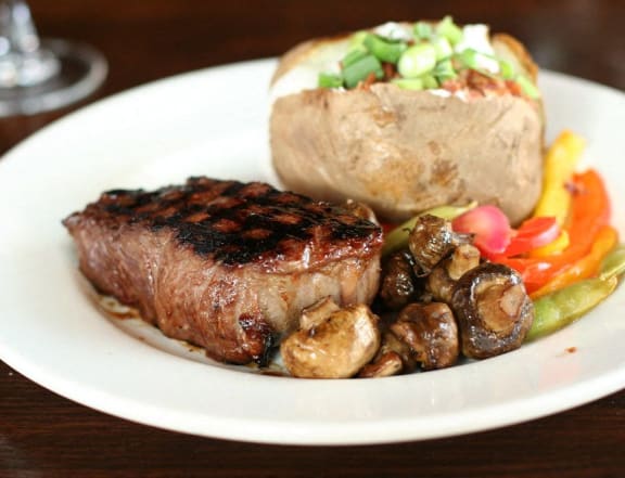 a plate of steak and a baked potato with mushrooms and vegetables