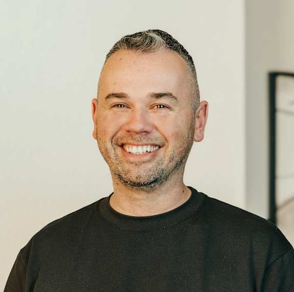A man with a beard and short hair is wearing a black shirt and smiling.