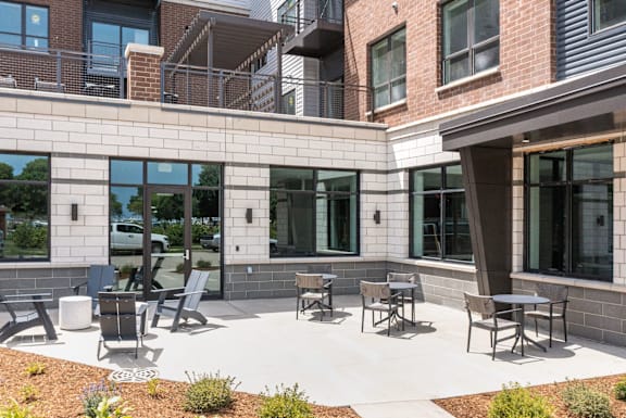 A patio with chairs and tables is surrounded by a brick building.