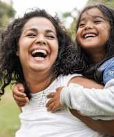 A woman and a young girl are laughing together in a park.