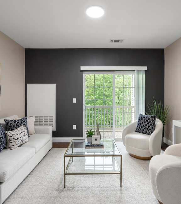 A modern living room with a white sofa, two white armchairs, and a glass coffee table.
