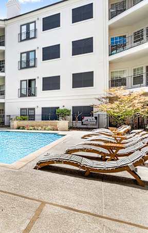 a swimming pool with chaise lounge chairs and an apartment building in the background