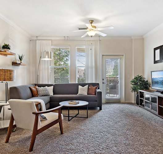 A living room with a grey couch, a white chair, a brown coffee table, and a flat screen TV.