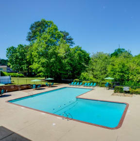 a swimming pool with chairs and umbrellas and trees in the background