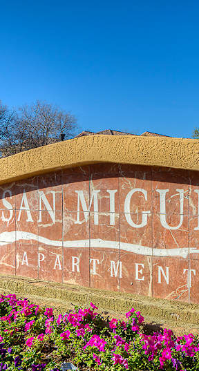 A sign that says San Clemente sits in front of a wall of flowers.