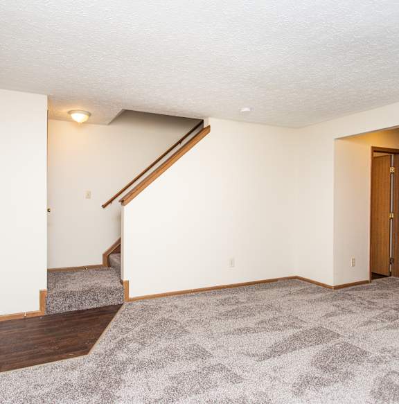 A room with a carpeted floor and a staircase leading to the second floor.