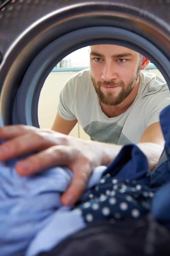 A man is looking at his clothes inside a washing machine.
