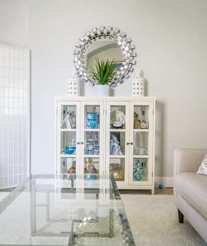 a living room with a glass coffee table and a white cabinet with glass doors