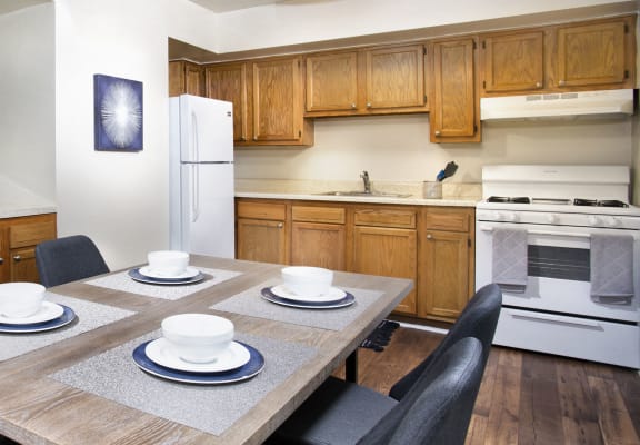 kitchen at Oaks at Park South apartments in Oxon Hill with plan flooring, white appliances, brown wood cabinets and dining table with four place settings