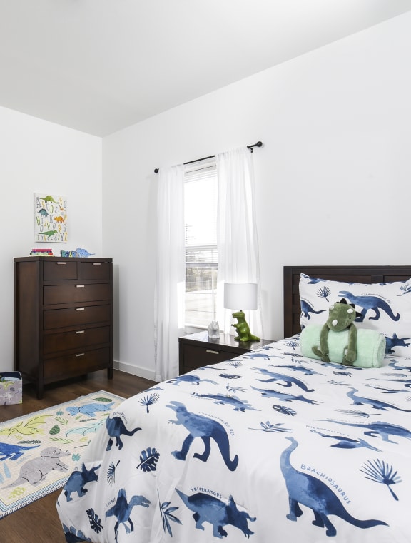 a bedroom with a bed with blue and white sheets and dinosaur bedding