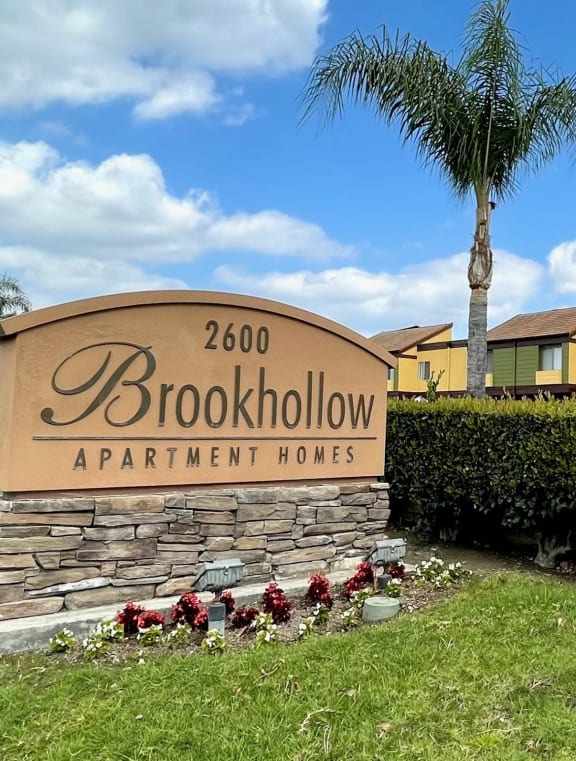 a sign apartment houses in front of a green lawn with flowers at Brookhollow Apartments, West Covina ,California, 91792