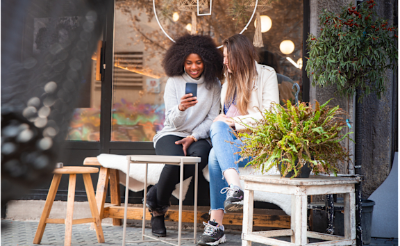 Two women sitting on a bench looking at a cell phone