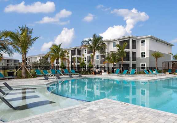 A large swimming pool surrounded by palm trees and lounge chairs. at Lucie at Tradition Apartments, Port St. Lucie, FL
