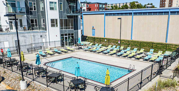 A pool surrounded by a black fence with chairs around it.