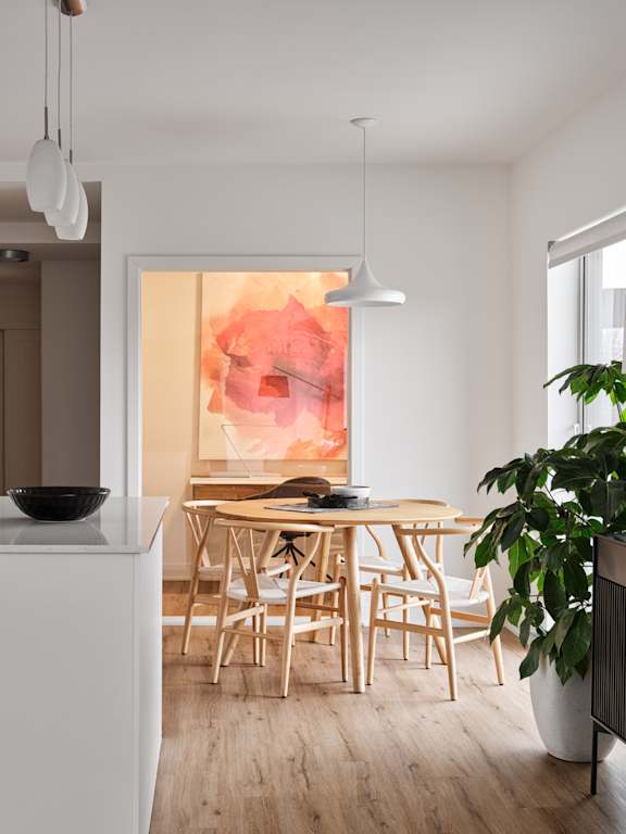 A modern kitchen with a white island and wooden chairs.