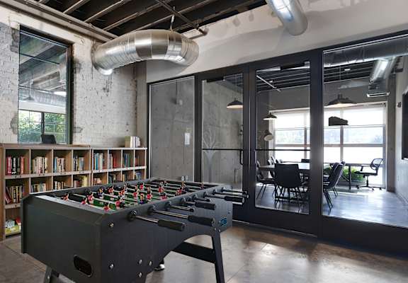 A foosball table is in the middle of a room with a brick wall and a bookshelf.