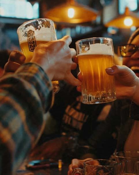 people sitting at a bar holding up glasses of beer