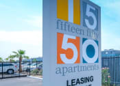 Thumbnail 23 of 23 - Fifteen Fifty apartments in Las Vegas modern concrete street sign at 1550 e Harmon Ave, Las Vegas, NV, 89119 on lush landscaping next to parking lot and gated apartments.