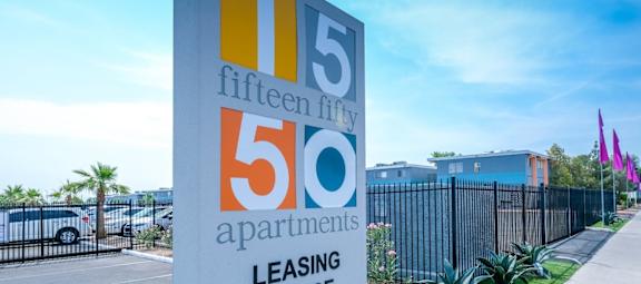 Fifteen Fifty apartments in Las Vegas modern concrete street sign at 1550 e Harmon Ave, Las Vegas, NV, 89119 on lush landscaping next to parking lot and gated apartments.