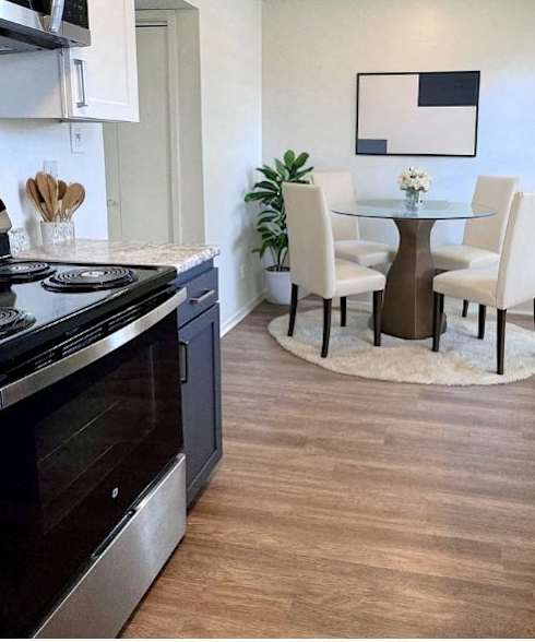 A kitchen with a black stove top oven and a round glass table with four chairs.