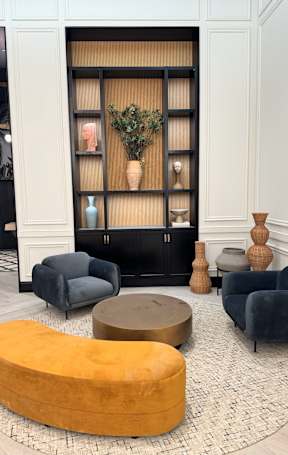 A living room with a grey sofa, a yellow ottoman and a black cabinet.