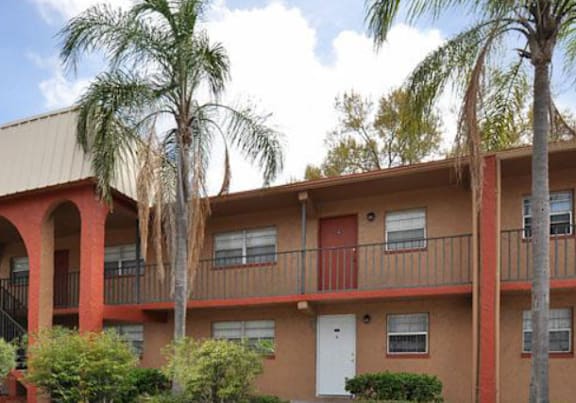 A building with a red and beige facade has a balcony and is surrounded by palm trees. at Oak Chase II, Tampa, 33612
