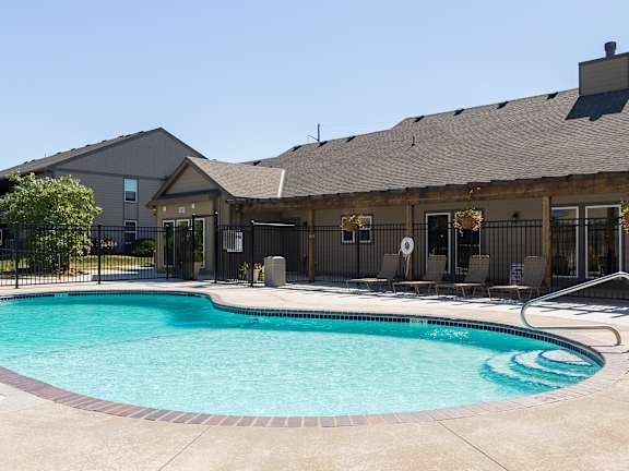 Community pool at Cedar Crest Apartments in Overland Park, KS, with sun loungers, umbrellas, and landscaped surroundings.